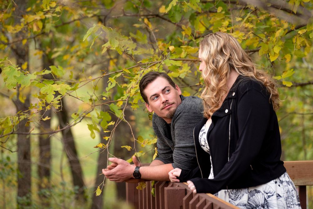 Couple sitting on bench under yellow autumn leaves in park setting.