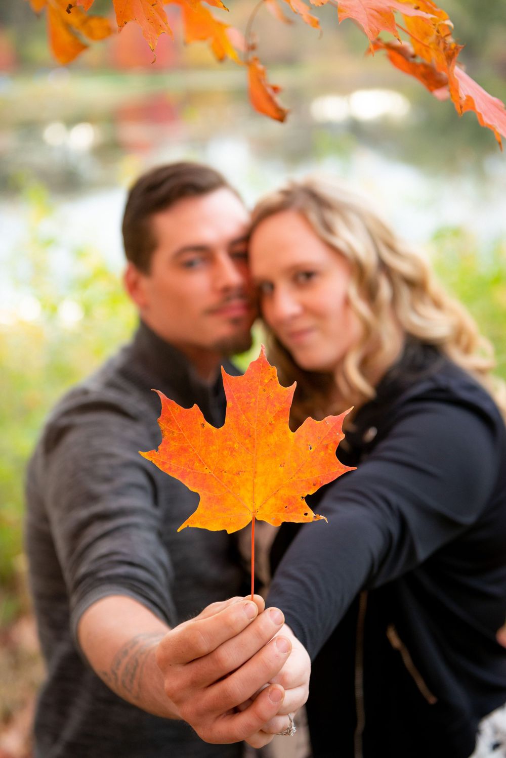 Bright orange maple leaf held up against blurred autumn background.