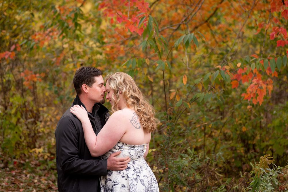 A romantic moment photographed in a park with bright red autumn leaves in the background.