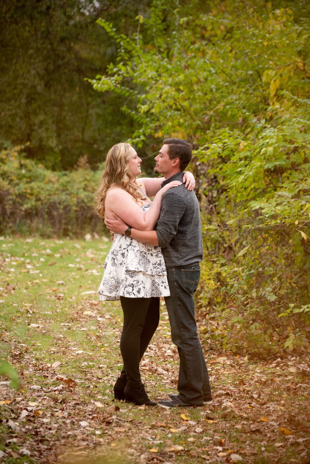 A couple's photoshoot on fallen leaves in a peaceful woodland setting.