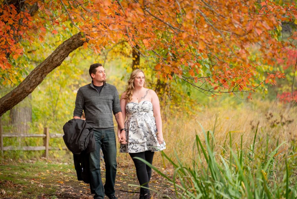 A couple walks together through a scenic autumn landscape with orange and yellow trees.