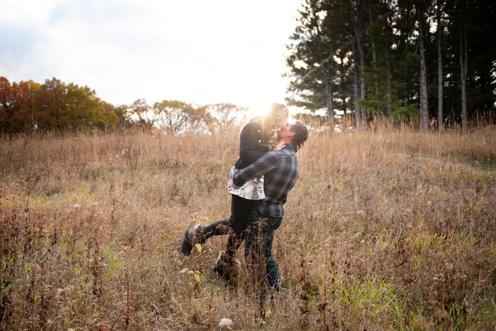 Couple embraces in a golden autumn field during sunset engagement photoshoot.