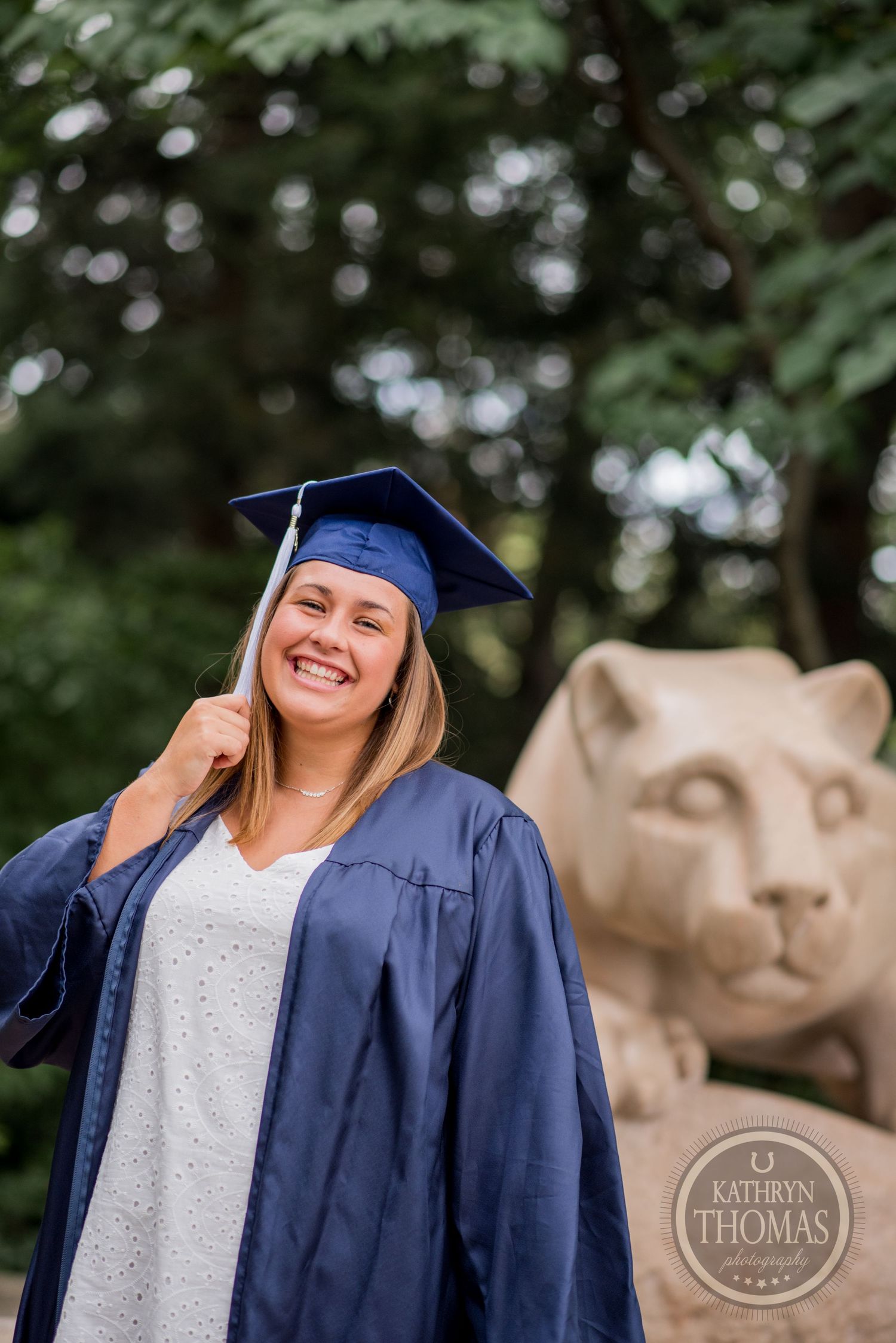 Happy graduate in blue cap and gown poses with Penn State's famous lion statue.