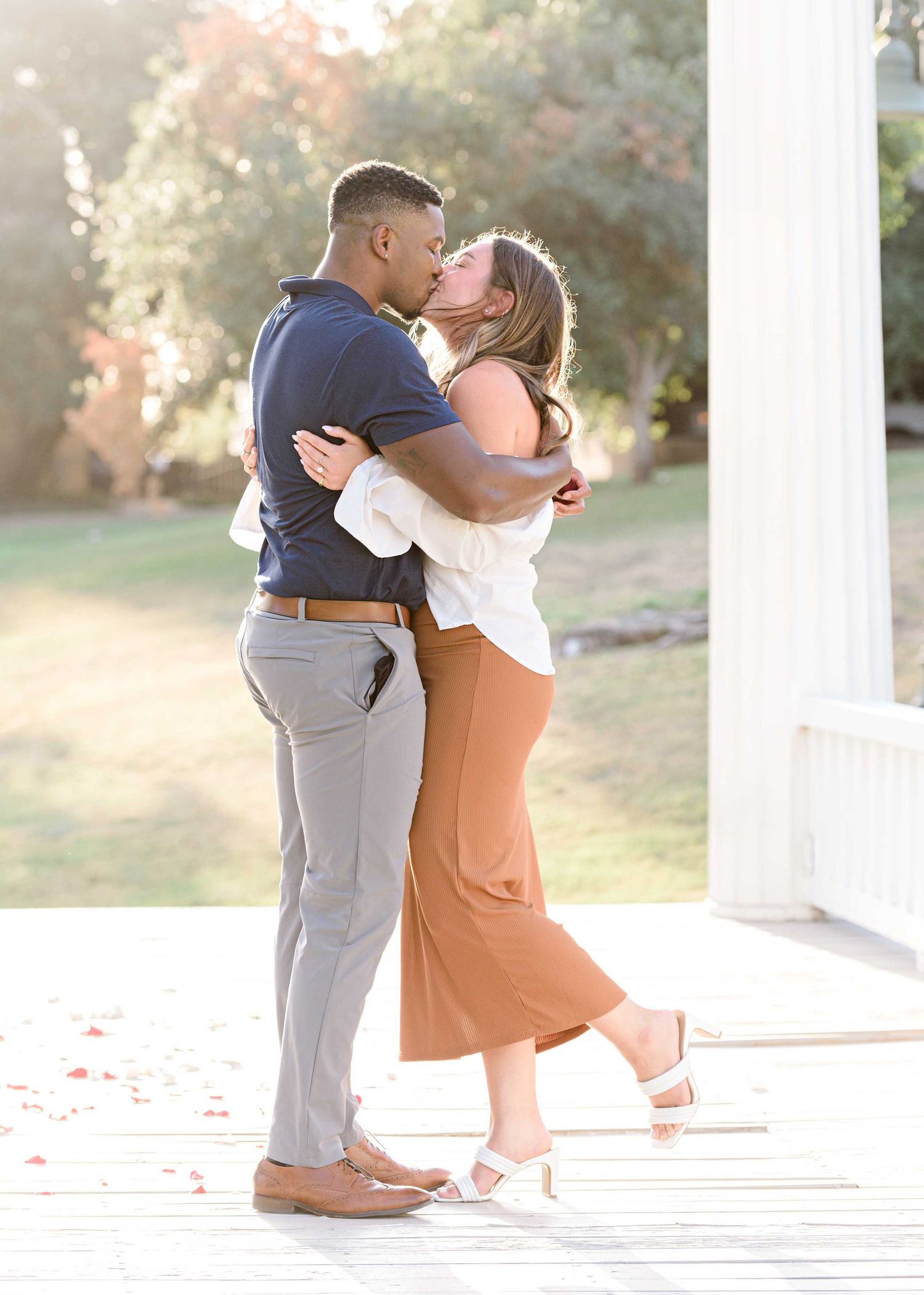 A romantic embrace under a white gazebo during golden hour.