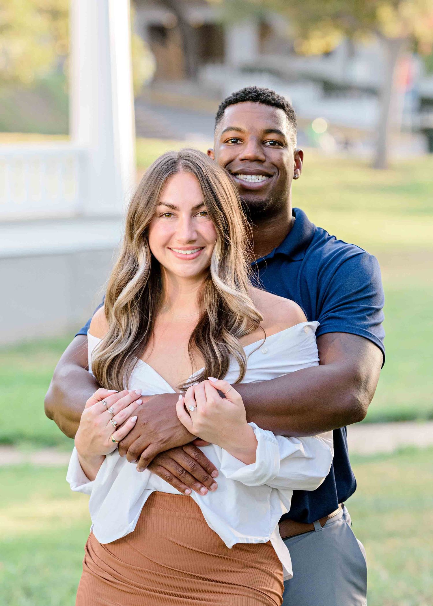 A romantic couple embraces outdoors wearing coordinated blue and white outfits in a sunny park setting.