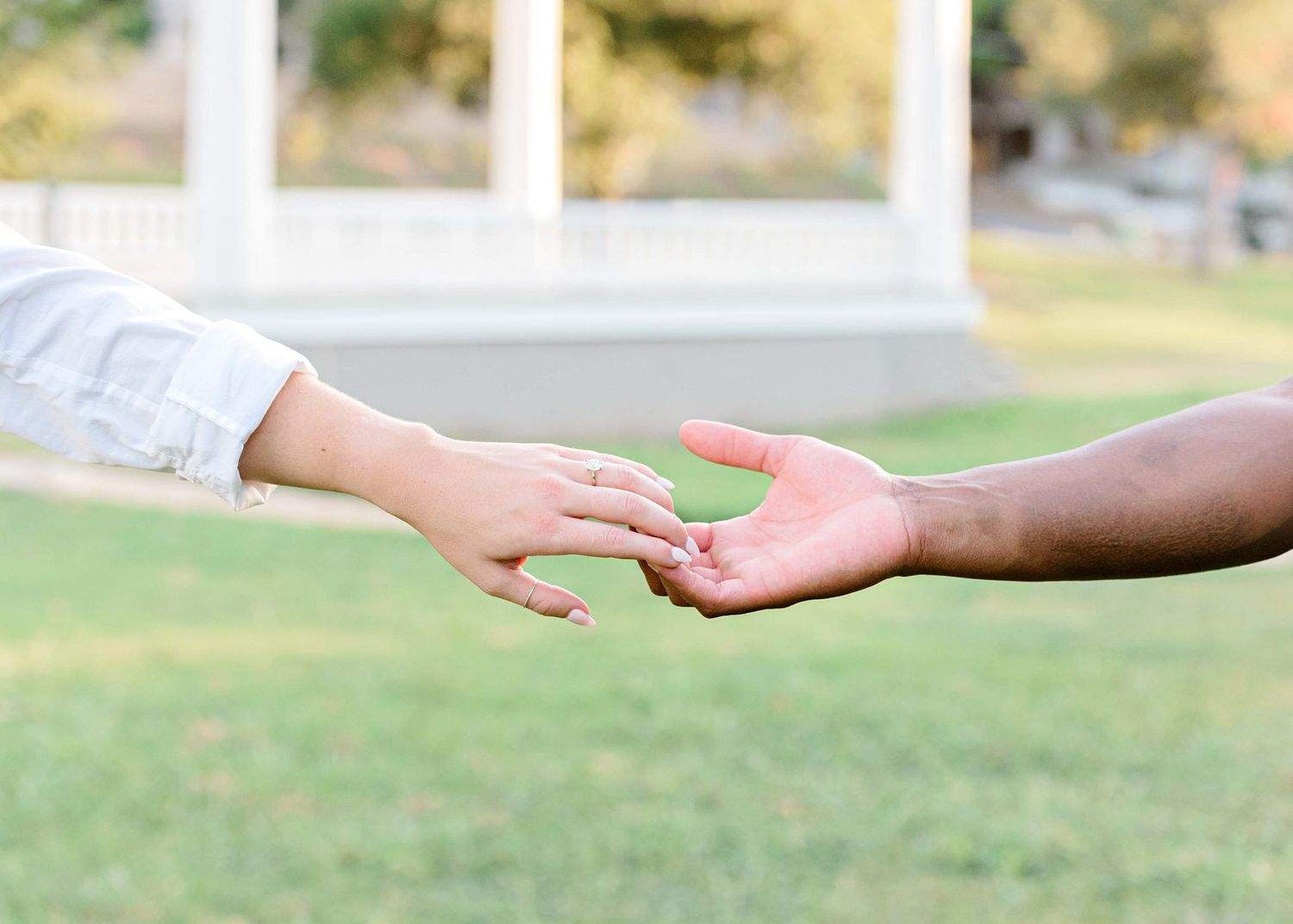 Two hands reaching towards each other against a sun-lit outdoor background.