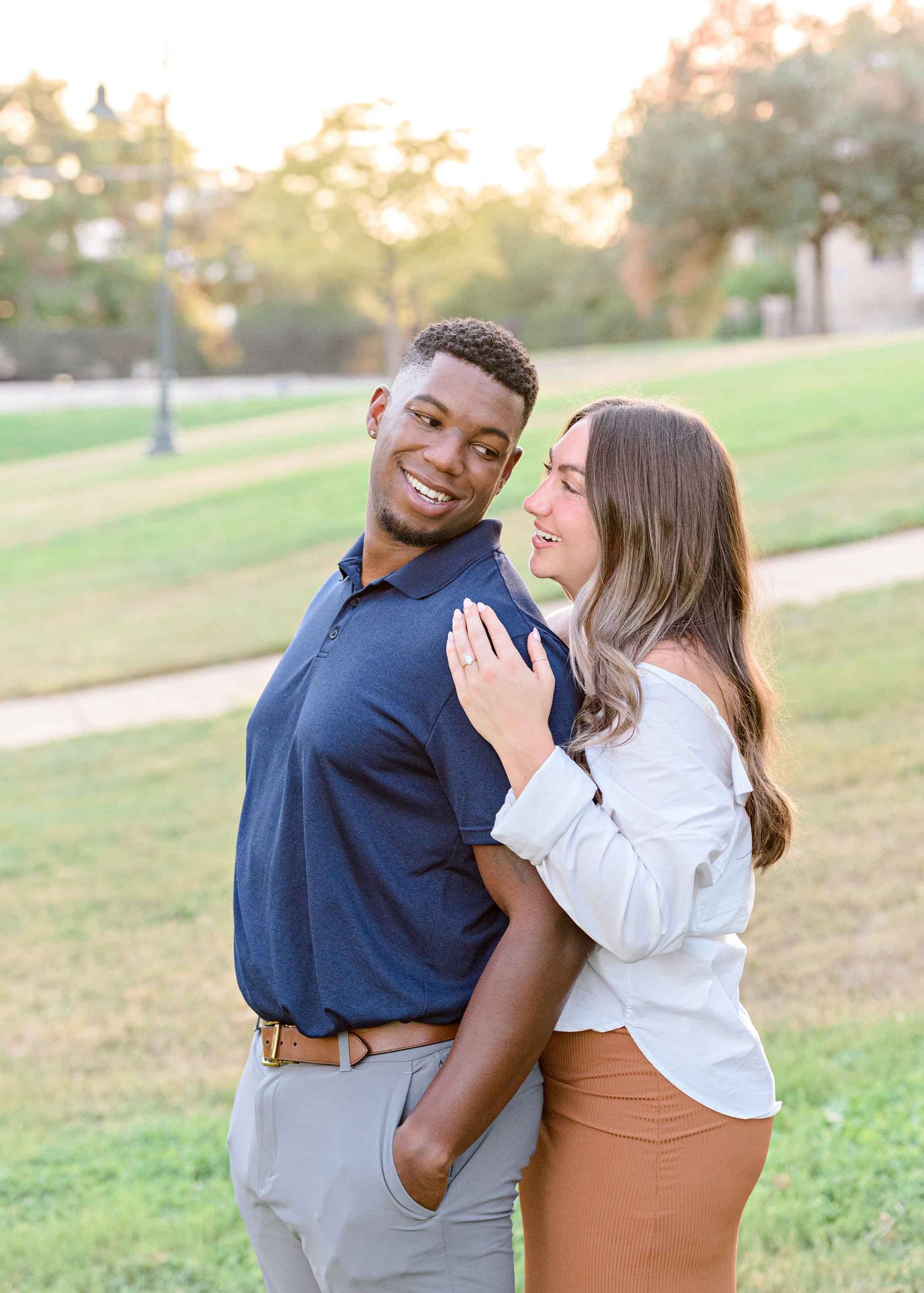 Happy couple poses together on a grassy hill during golden hour engagement photos.