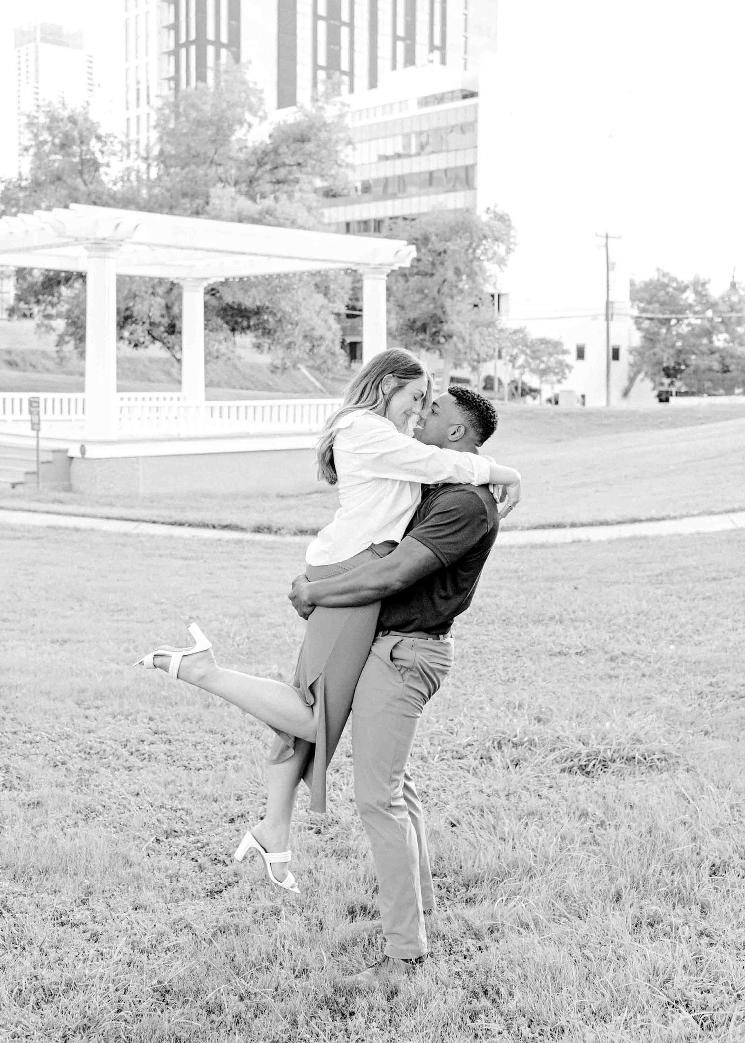 A joyful black and white photo of a couple embracing and lifting each other on grass.