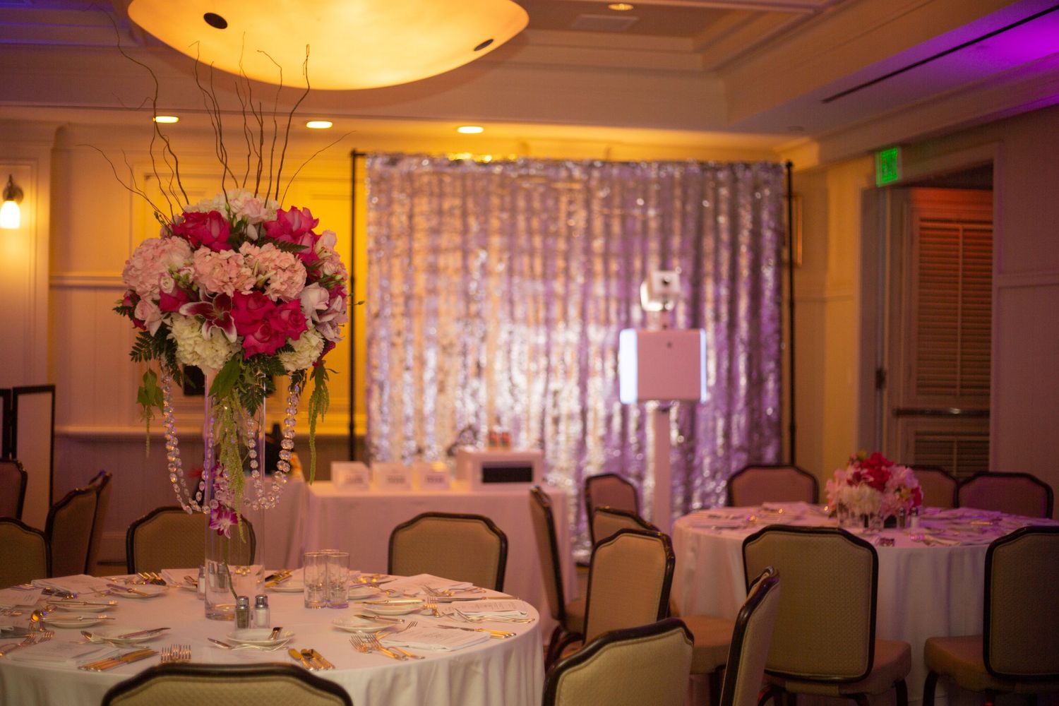 Elegant wedding reception venue with tall floral centerpieces, white tablecloths and purple mood lighting.
