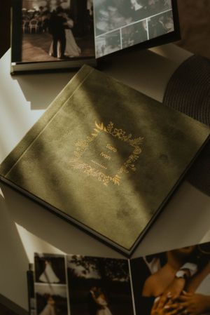 Professional wedding album with gold embossed design displayed among scattered photographs.