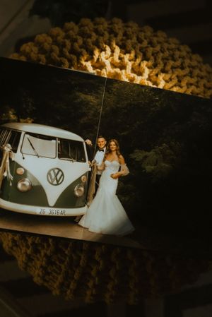 Wedding photo showing couple posing with classic VW bus through knitted textile frame.