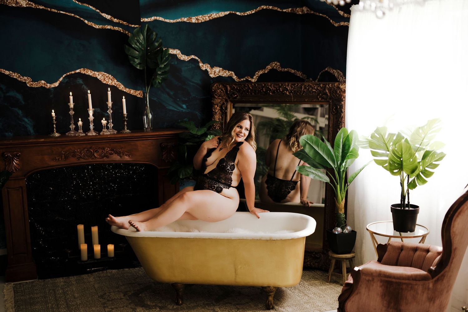 Confident woman lounging in a vintage bathtub, smiling playfully, surrounded by plants and a decorative fireplace.