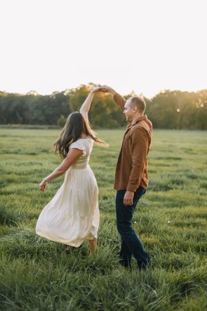 Couple dancing playfully in a grassy field during sunset.