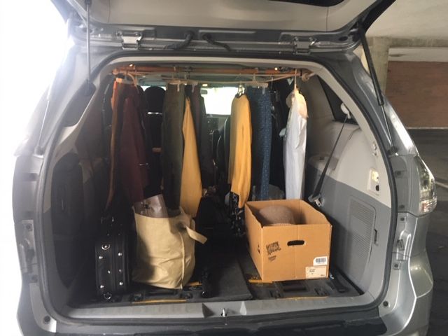 Car trunk packed with clothing on hangars and storage boxes for transport.