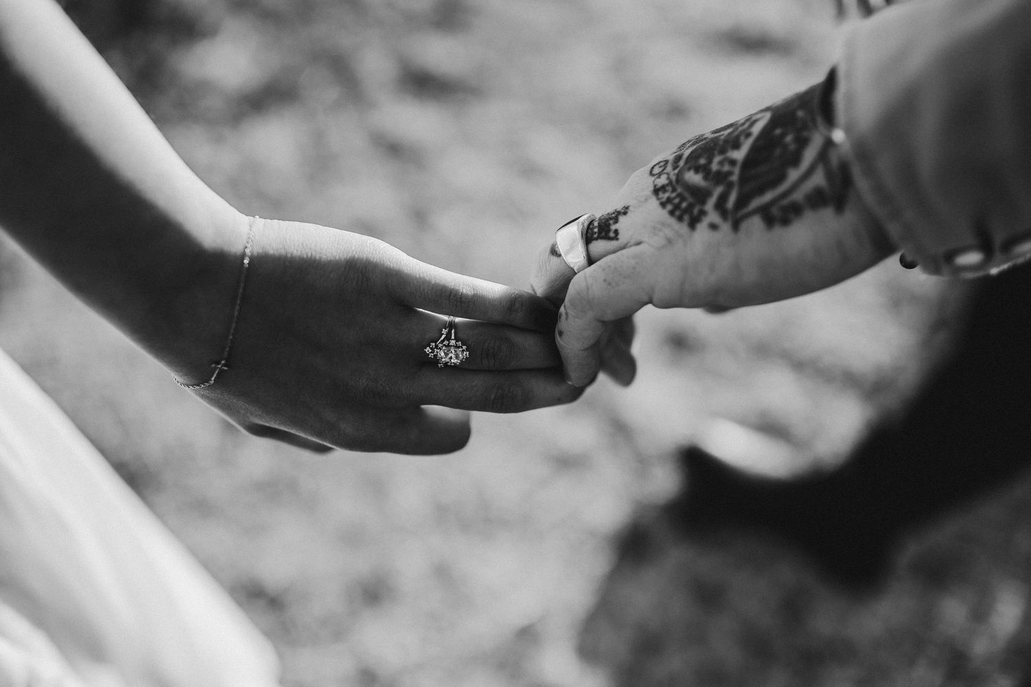 Close-up black and white shot of two hands touching with visible tattoos and rings.