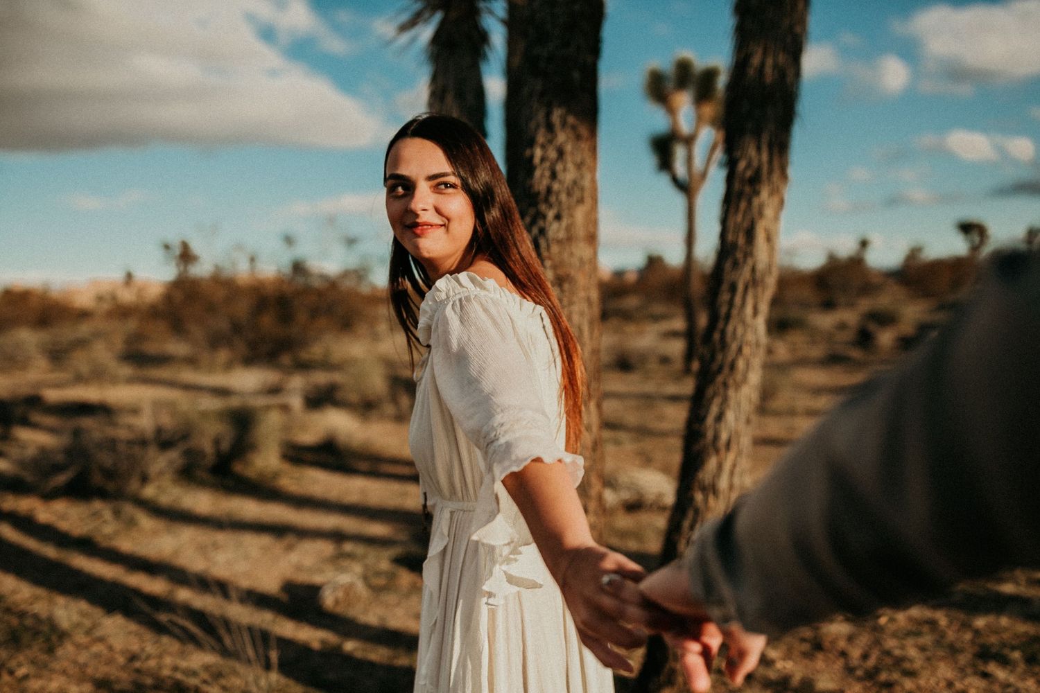A couple holding hands in a sunlit Joshua Tree desert setting.