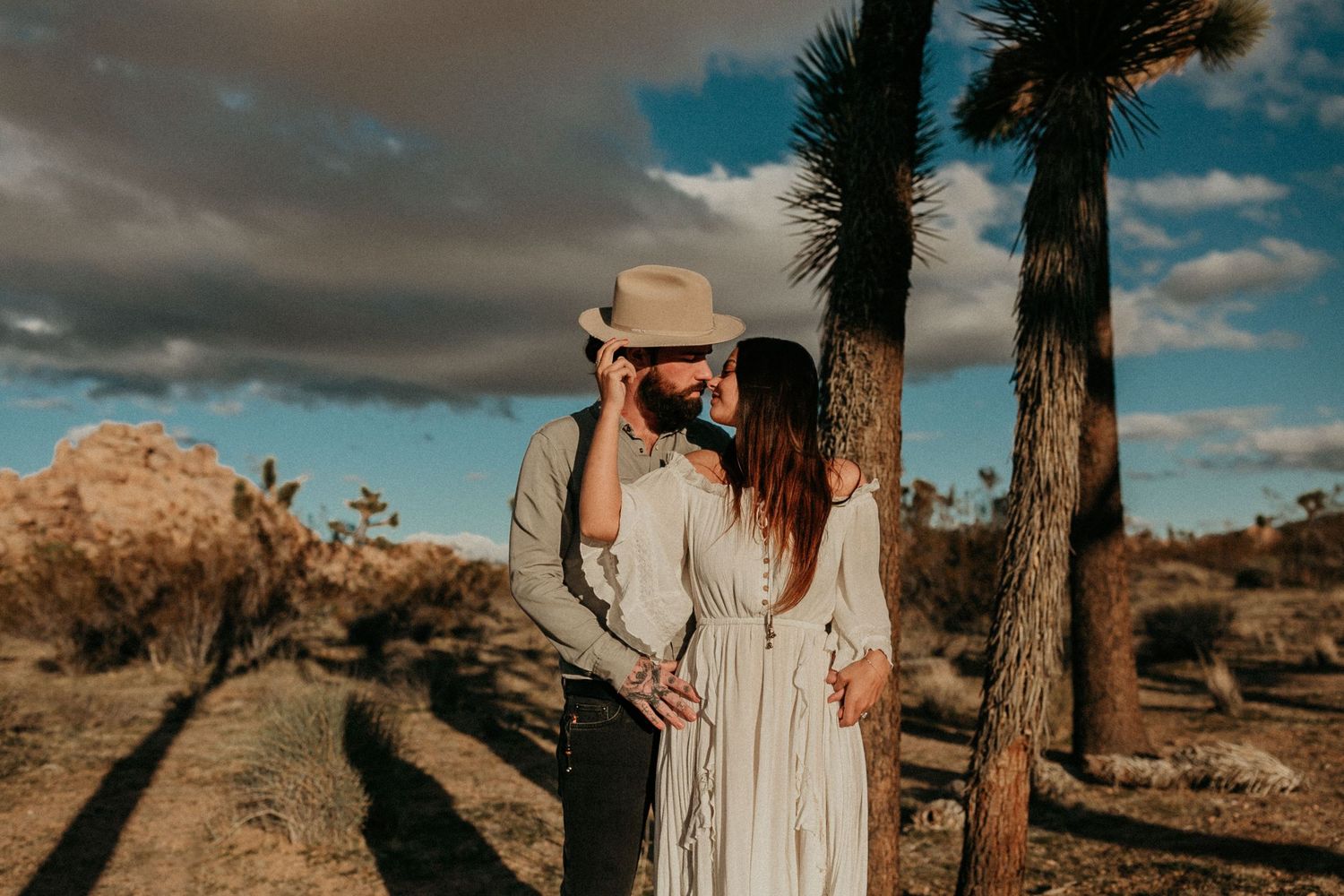A romantic desert engagement session with Joshua Trees and moody skies in the background.