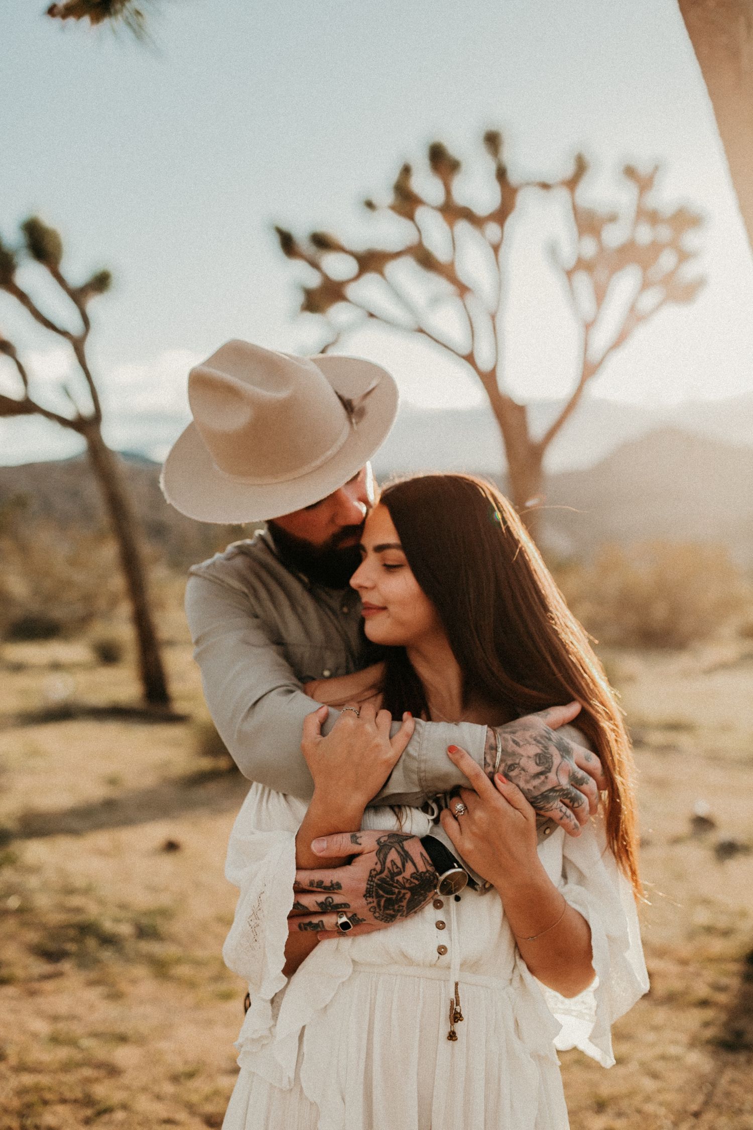 A tender embrace in the desert with Joshua Trees silhouetted against the sky.
