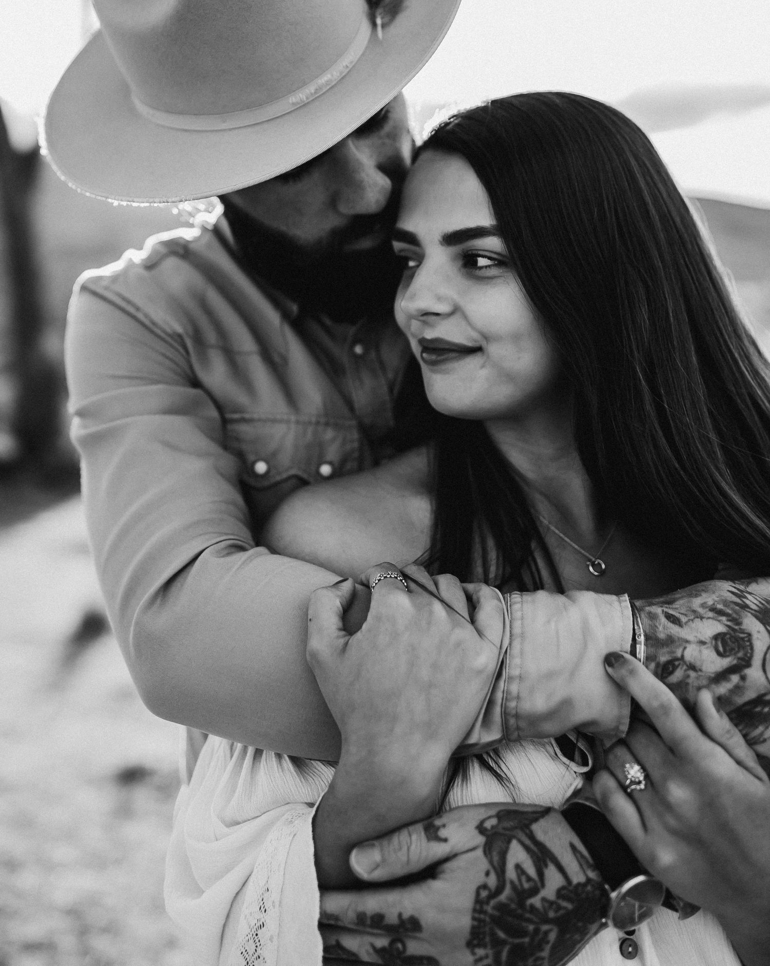 Monochrome portrait capturing an intimate embrace between two people in western style attire.