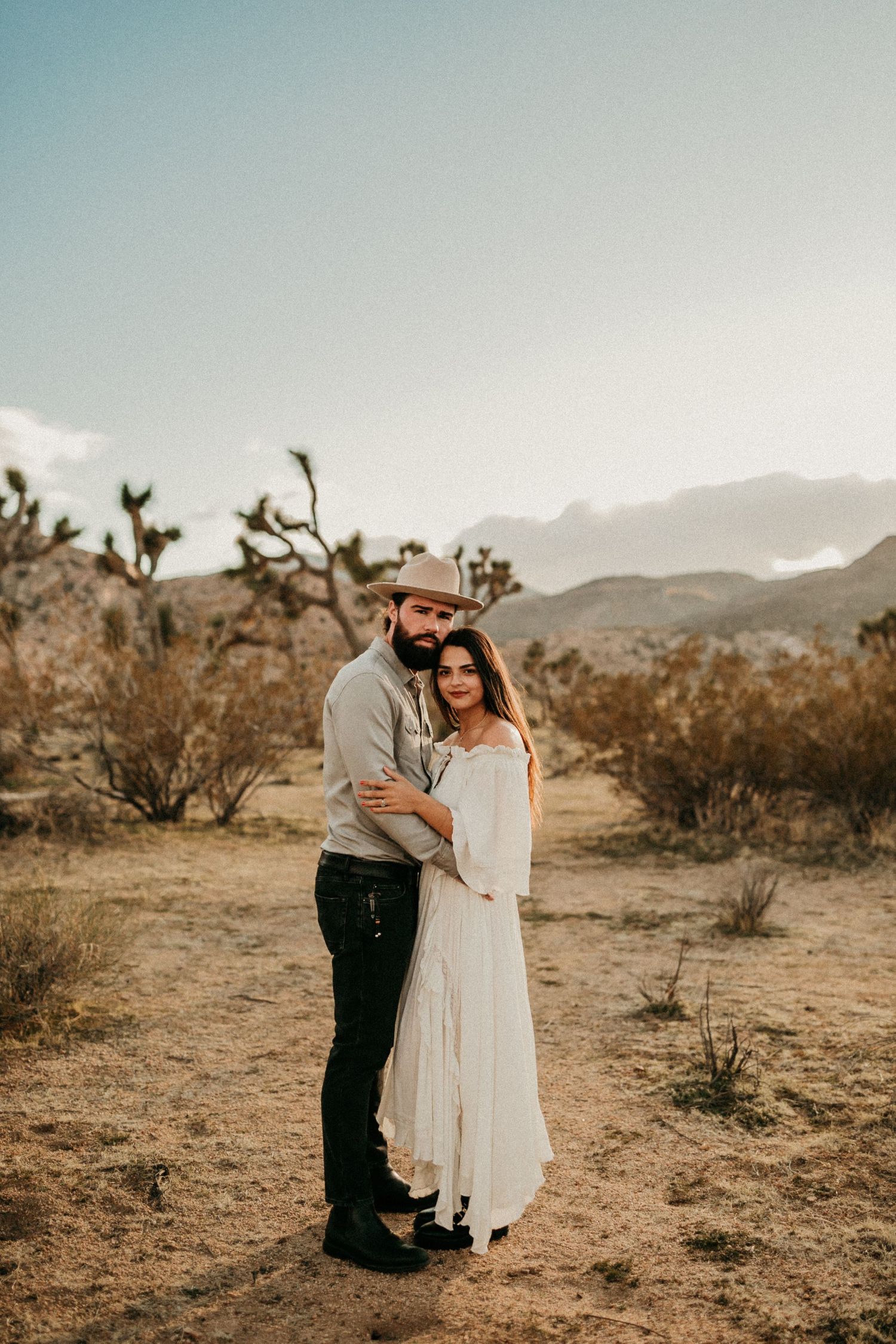 Romantic couple embracing in desert landscape during sunset with mountains in background.