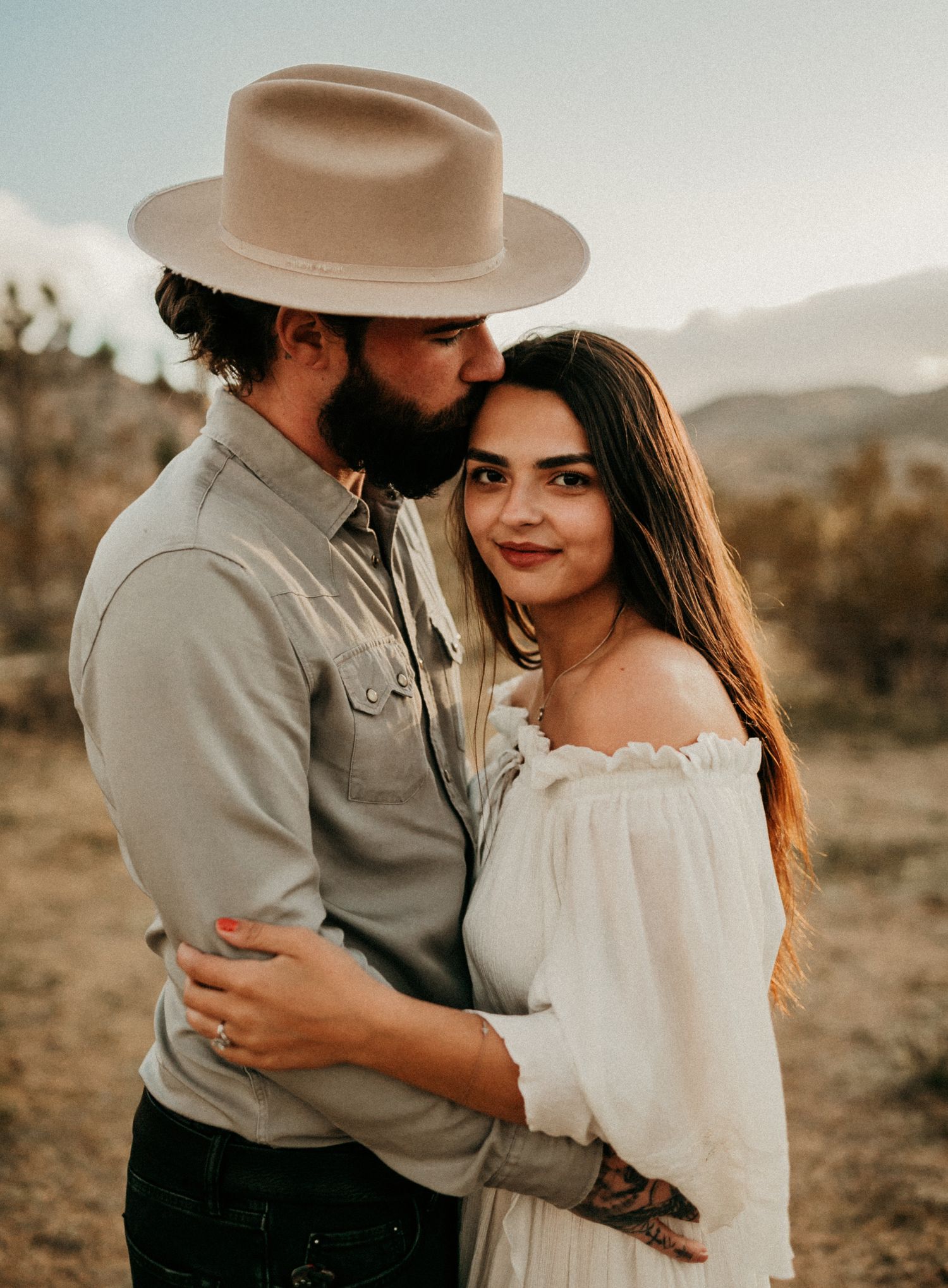 Romantic desert engagement photo with couple in western style attire at golden hour.