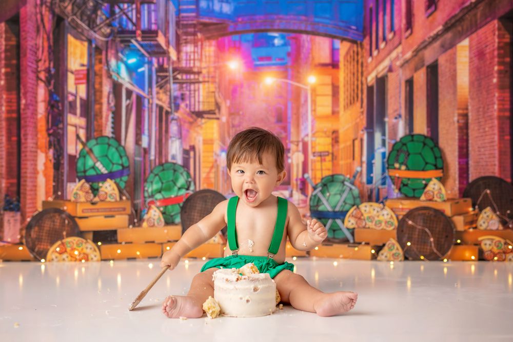 Baby in green outfit against cityscape backdrop during studio photoshoot.