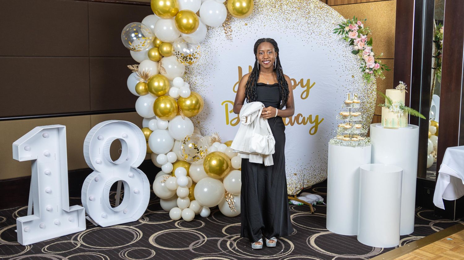 Elegant party setup with white and gold balloon arch, number 18 lights, and decorative columns.