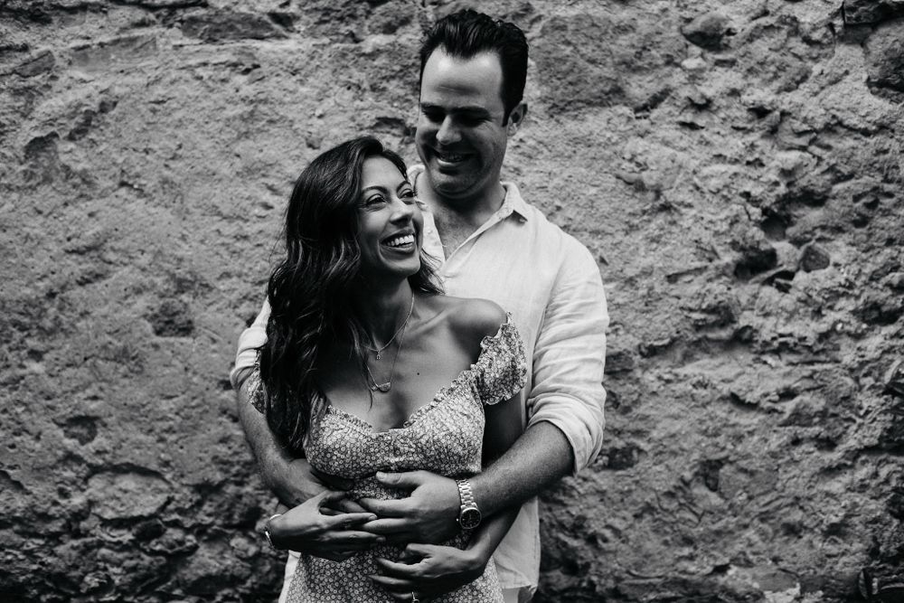 A joyful candid black and white moment captured against a weathered stone wall background.