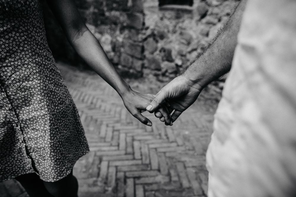A black and white close-up of two hands touching against a brick patterned background.