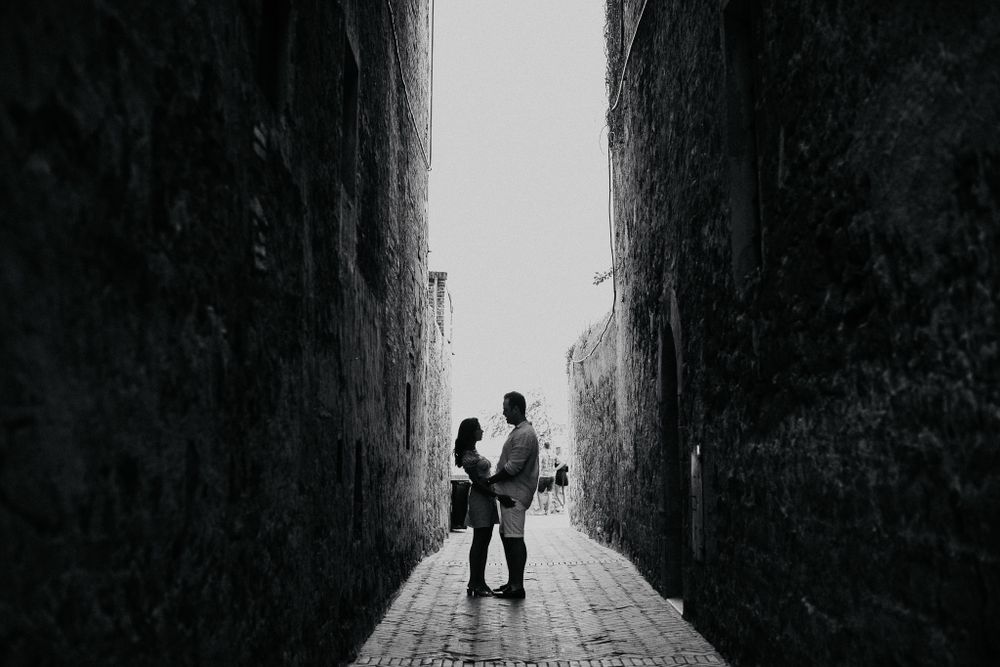 A silhouetted couple standing in a narrow alleyway between tall stone walls.