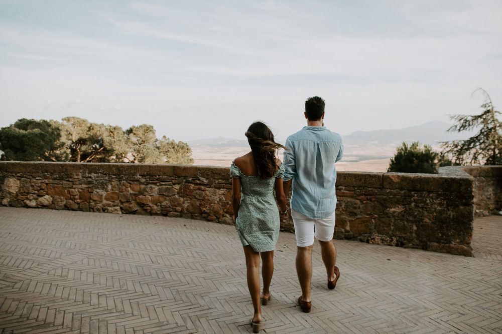 A couple walking along a stone wall overlooking a scenic landscape at sunset.