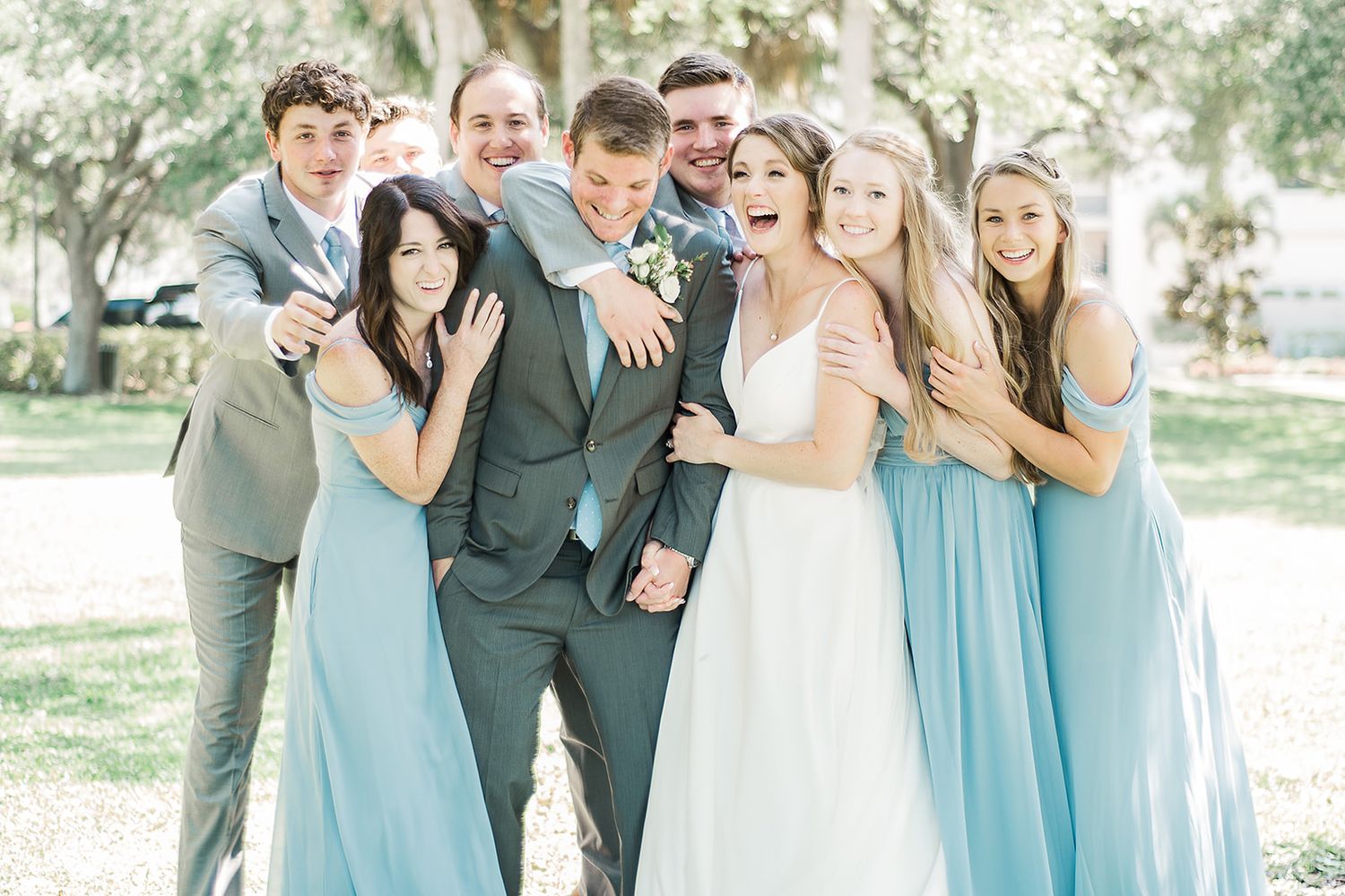 Wedding party poses playfully in light blue dresses and grey suits.