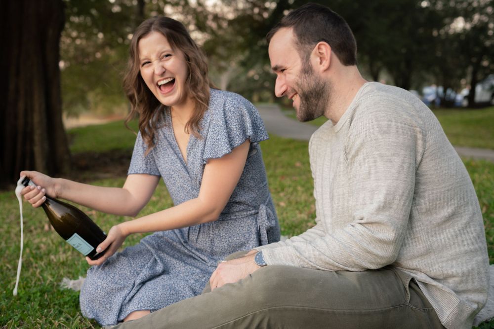 A couple laughs together while opening champagne during their outdoor celebration.
