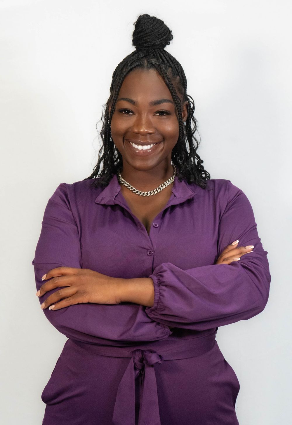 Smiling woman in purple outfit with braided hair and silver necklace posing confidently.