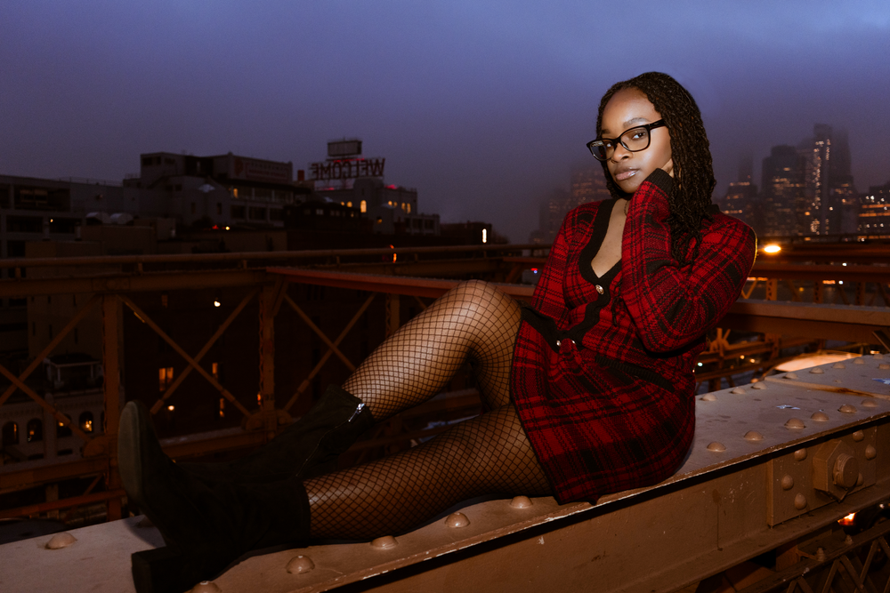 A nighttime portrait on a bridge with city lights and red plaid outfit.