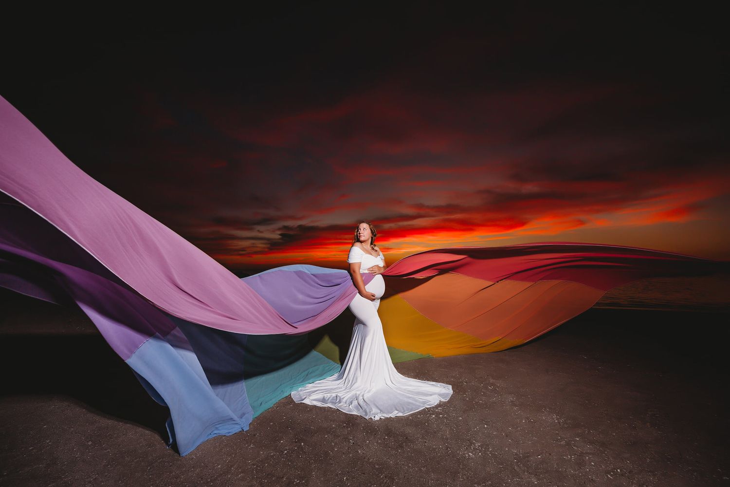 Dramatic sunset photo with flowing purple and red fabric against dark sky and desert landscape.