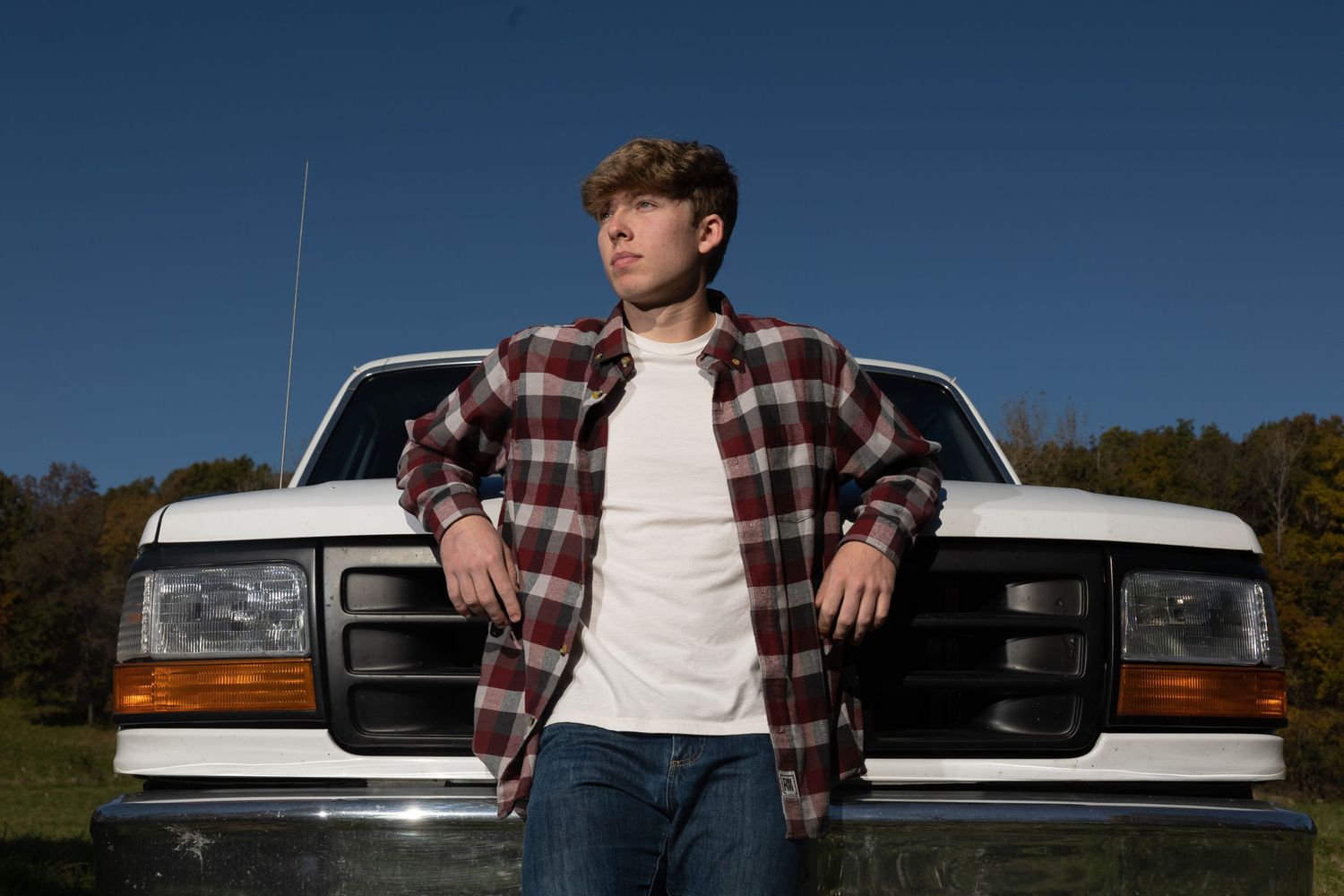 A Charleston, Illinois high school senior boy leans against the front of his white truck for his senior pictures.