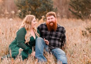 Couple sitting together in tall grass field during autumn wearing casual clothing.