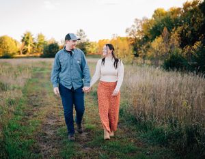 A couple takes a romantic walk together through a golden autumn field at sunset.