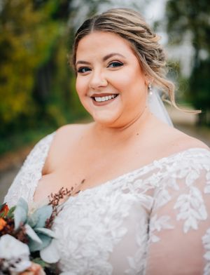 Bride in lace gown smiles while holding autumn bouquet with eucalyptus and orange flowers.
