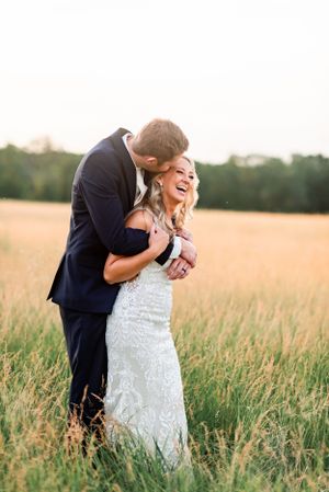 Joyful wedding couple laughing together in golden wheat field at sunset.