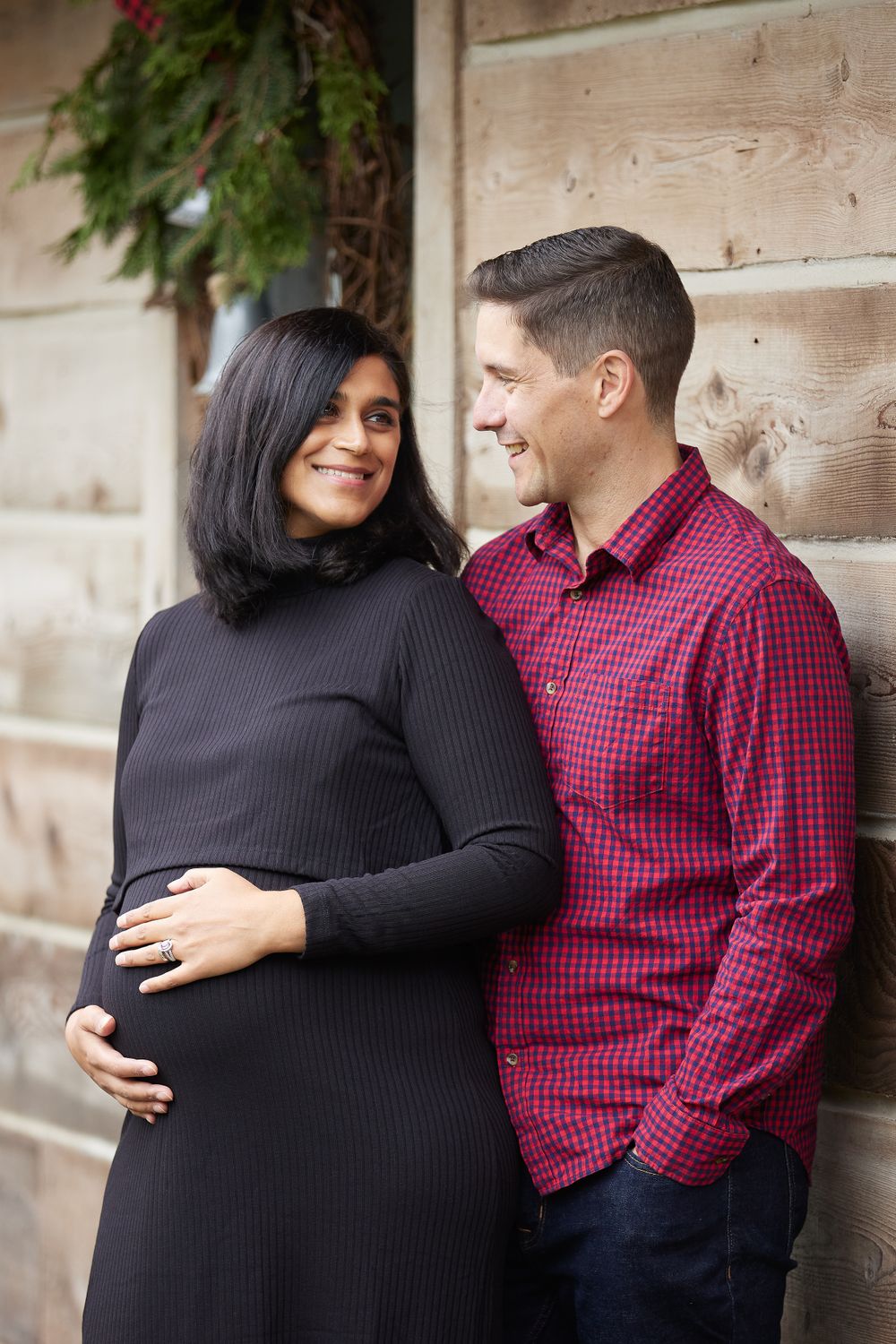 A close couple sharing an intimate moment against a wooden wall with holiday decor in the background.