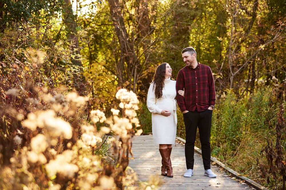 A couple walks together on a wooden boardwalk surrounded by golden autumn foliage at sunset.