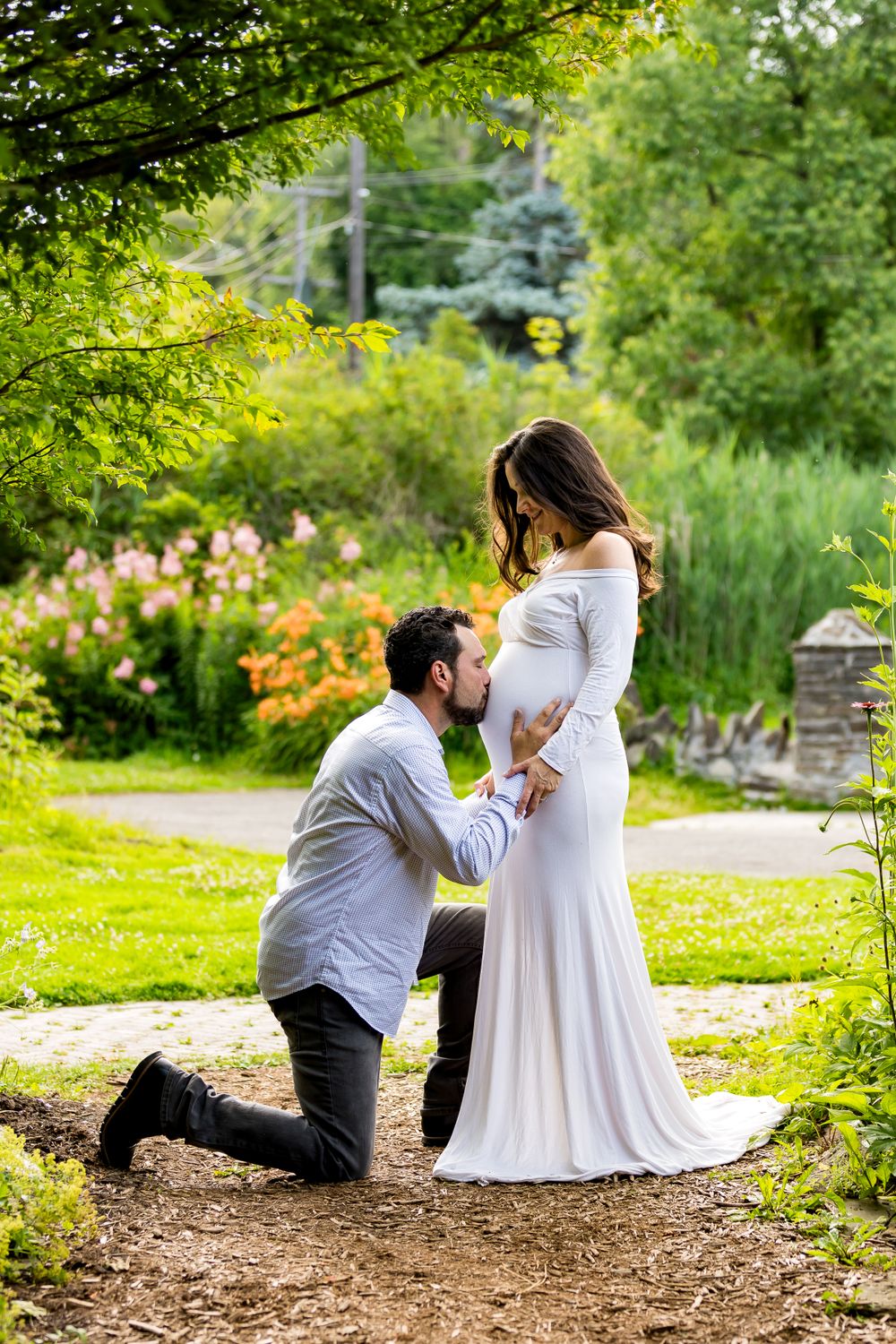 Husband kissing his wife's pregnant belly in a Summer Garden