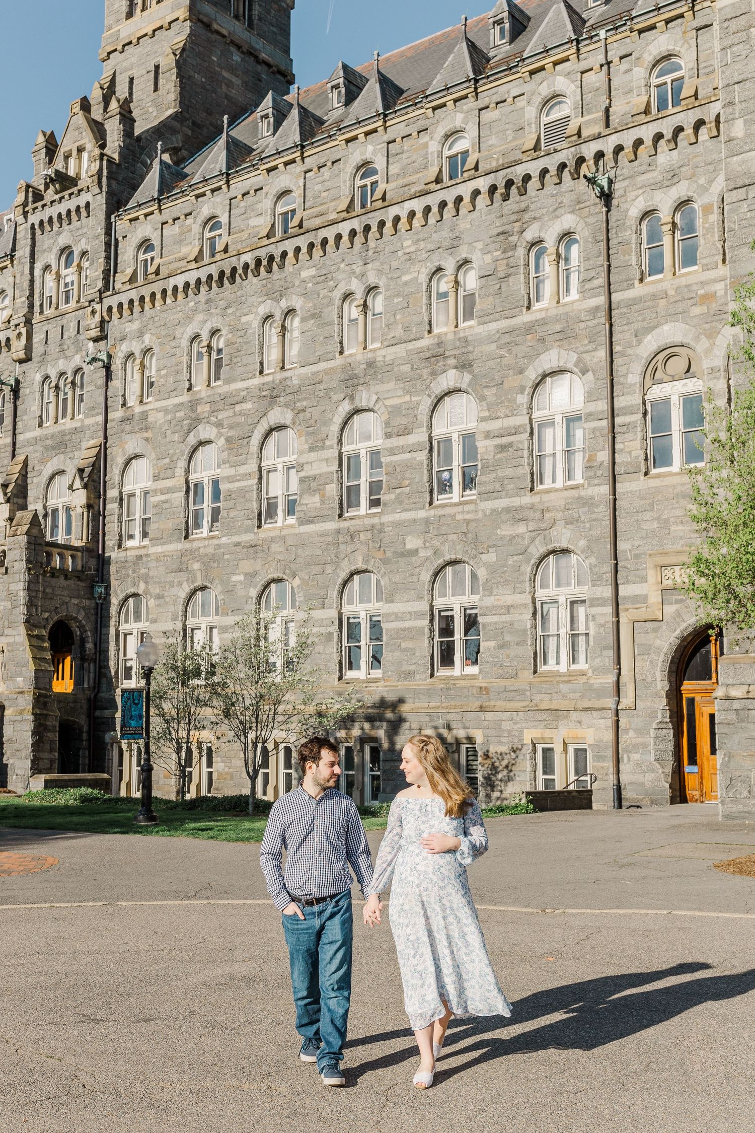 Two people walk along the front of a grand Gothic stone castle building.