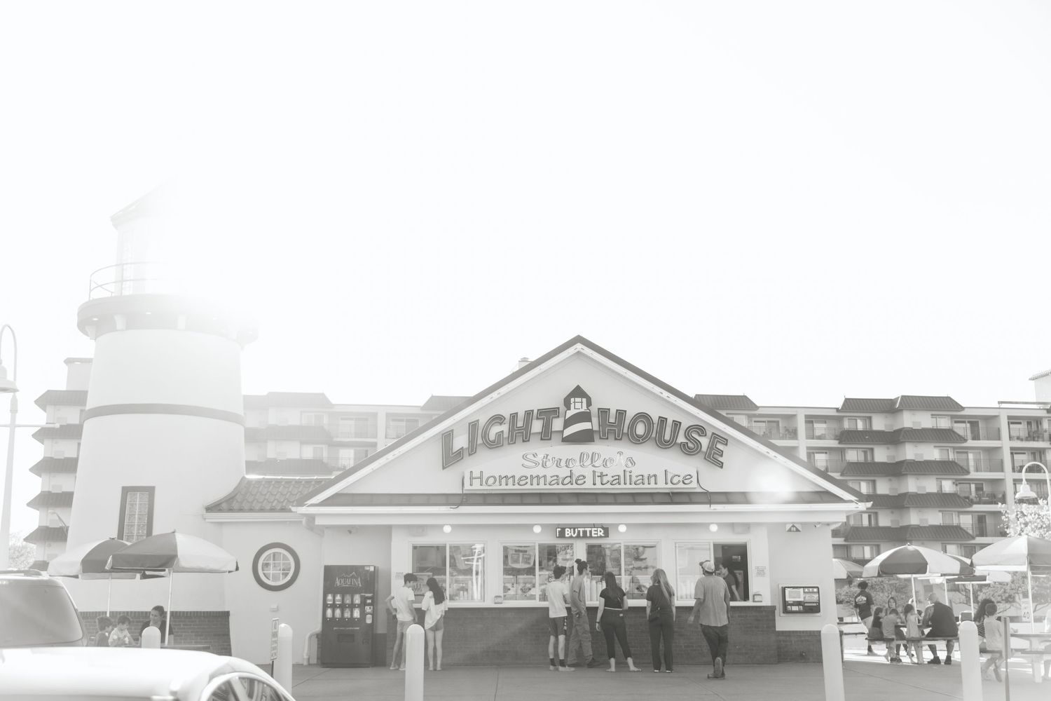 Black and white wide shot of Light2House homemade Italian ice shop with lighthouse tower and patrons.