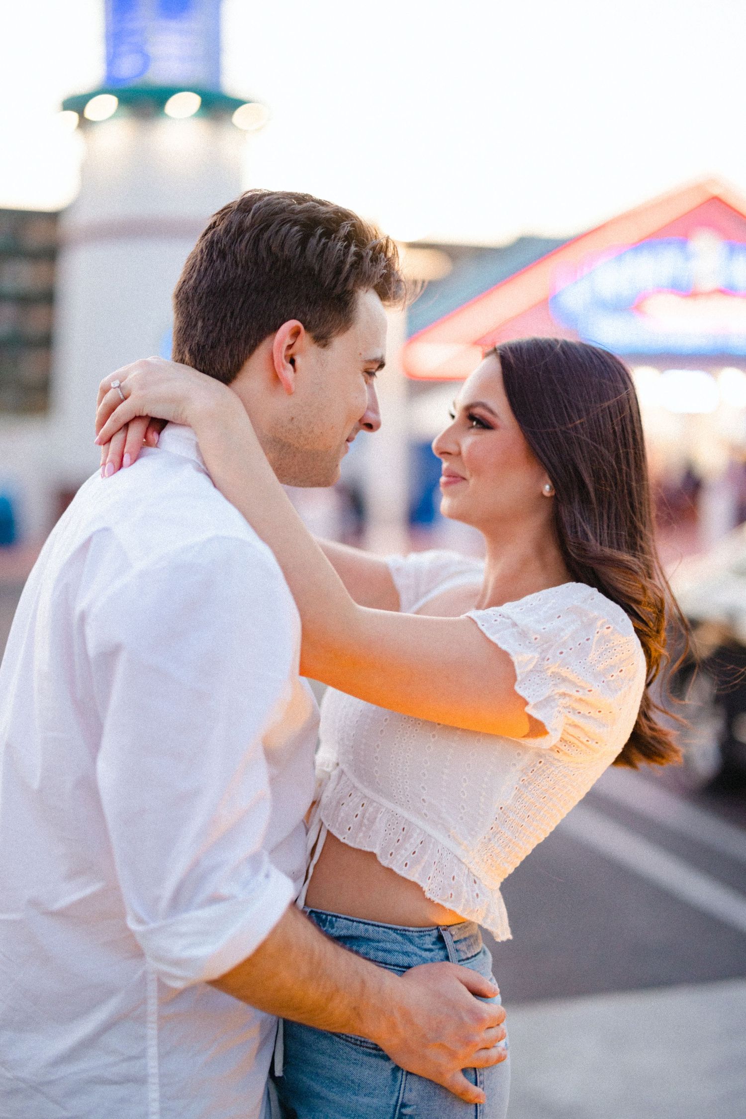 Couple embracing and gazing at each other warmly in golden hour light near colorful boardwalk shops.