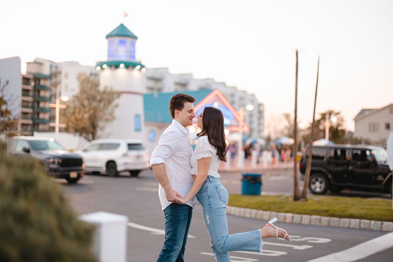 Couple holding hands and smiling at each other on a sunny boardwalk street near colorful buildings.