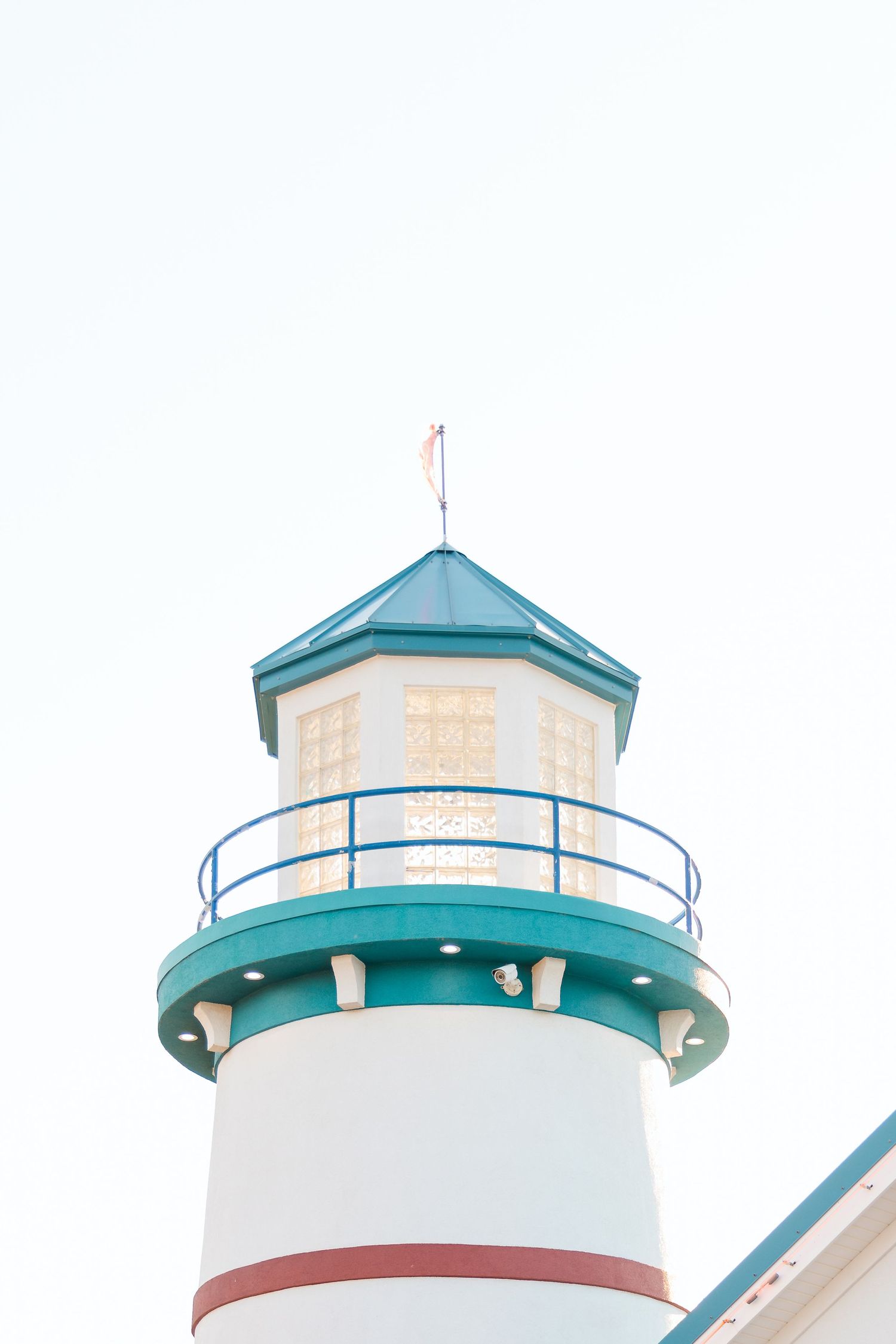 Close-up of decorative white and teal lighthouse replica with red flag on top against pale sky.