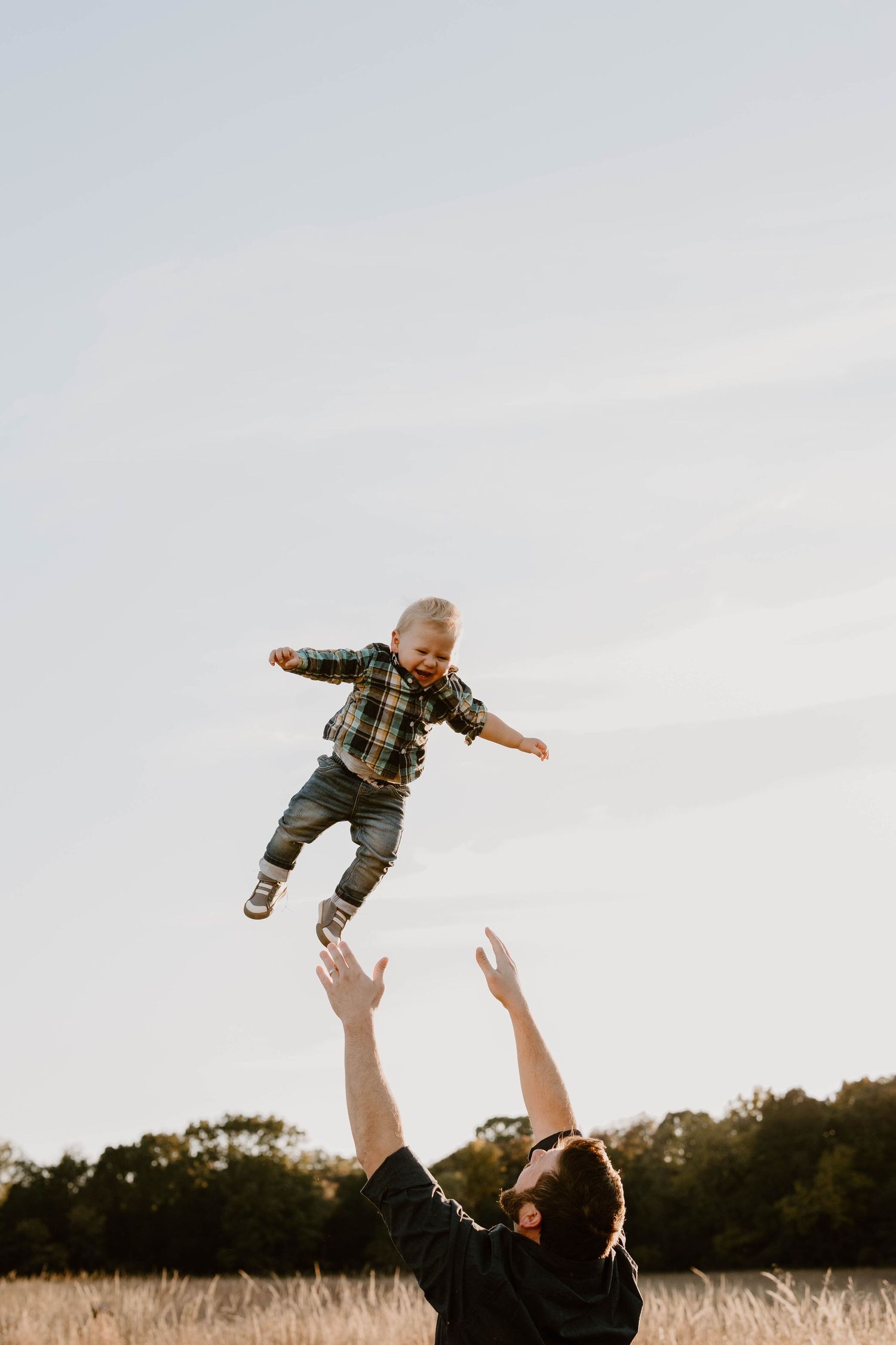 Person tossing child high in the air against cloudy sky in field.